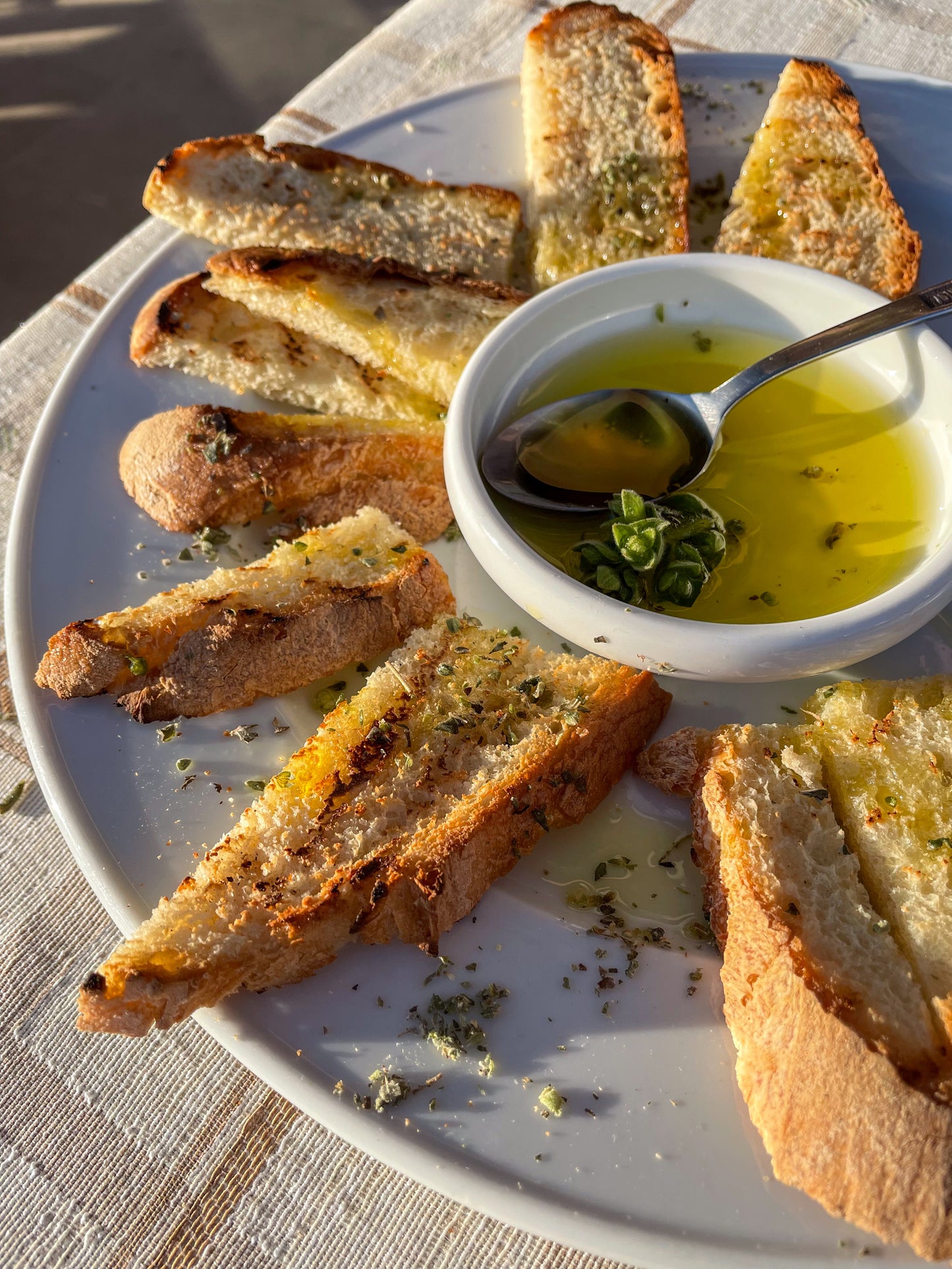 Plated bread slices with a bowl of olive oil and herbs on a textured surface