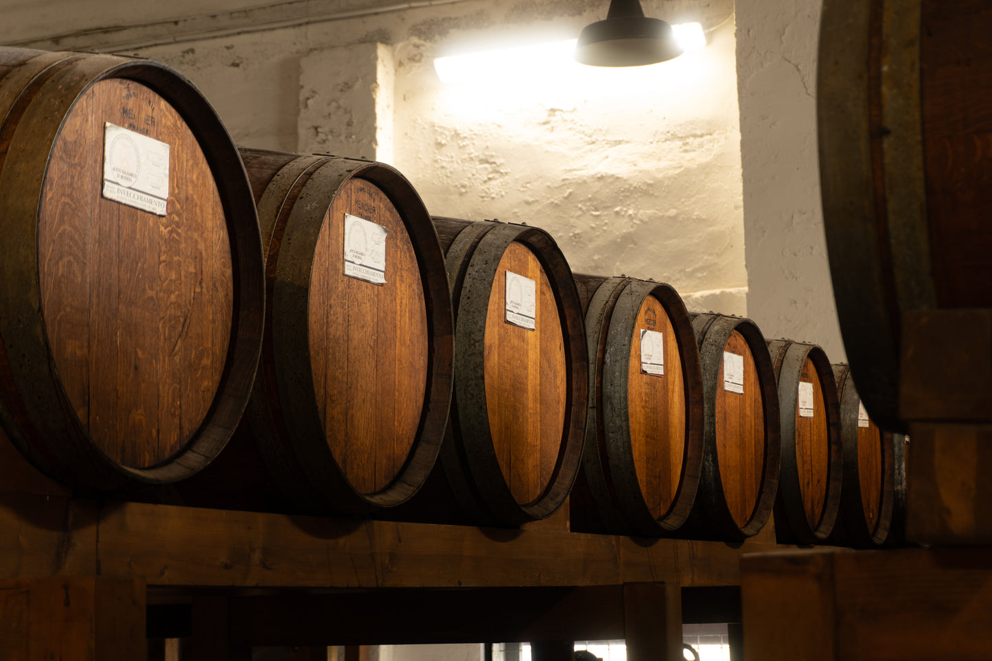 Row of wooden barrels containing balsamic with labels in a storage room.