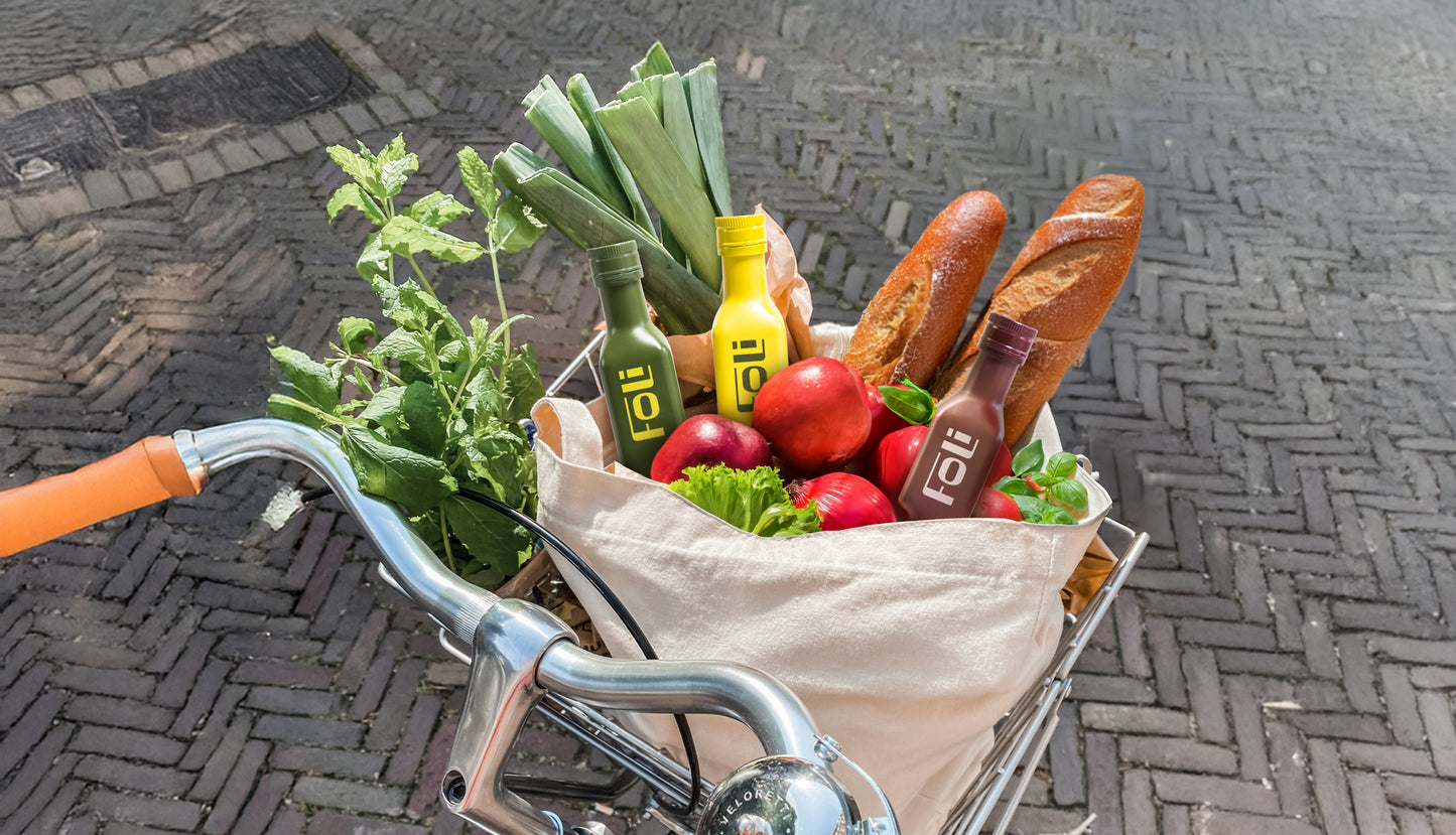 Basket of groceries on a bicycle handlebar with FOLI bottles with vegetables and bread