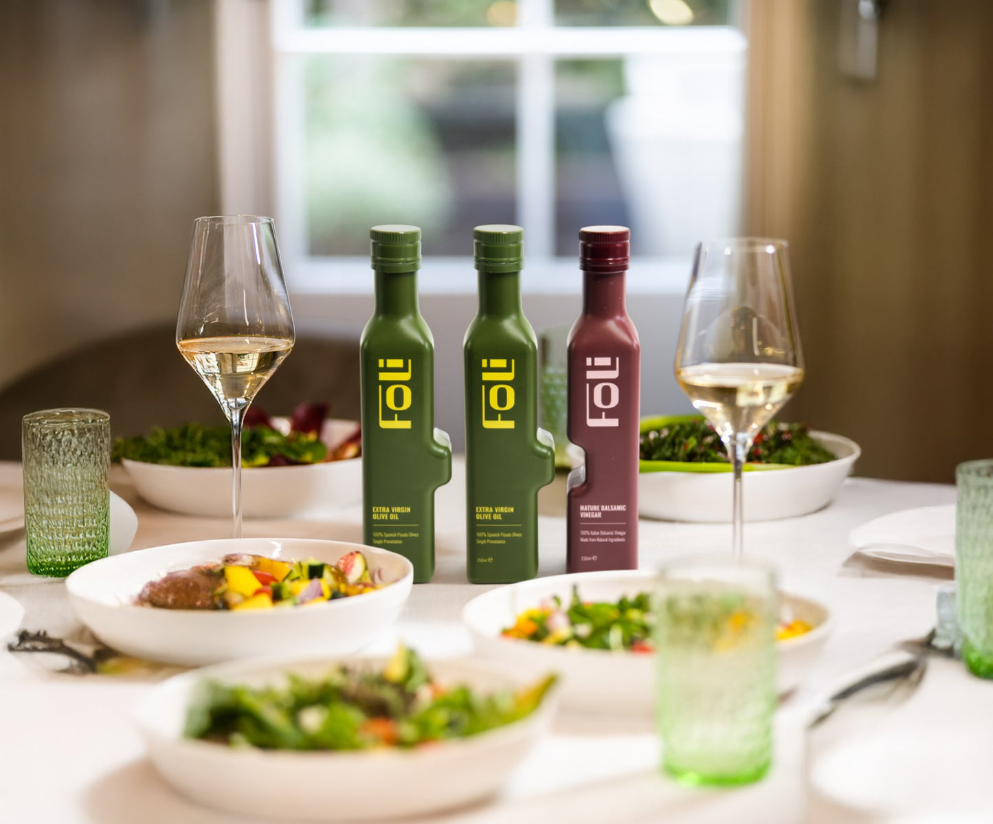 FOLI olive oil and balsamic vinegar bottles with glasses and salads on a table