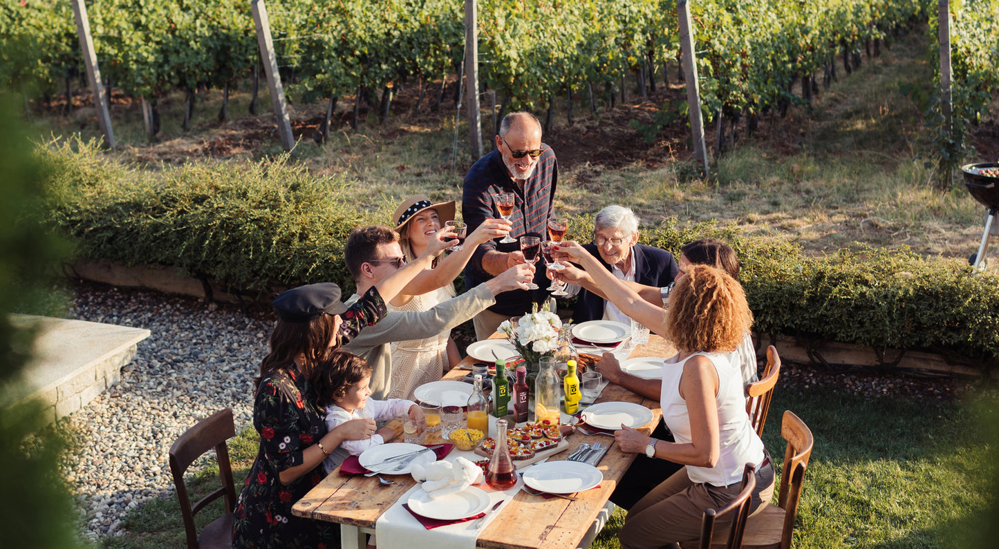 Group of people enjoying a meal with FOLI bottles on the table and toasting drinks outdoors in a vineyard 
