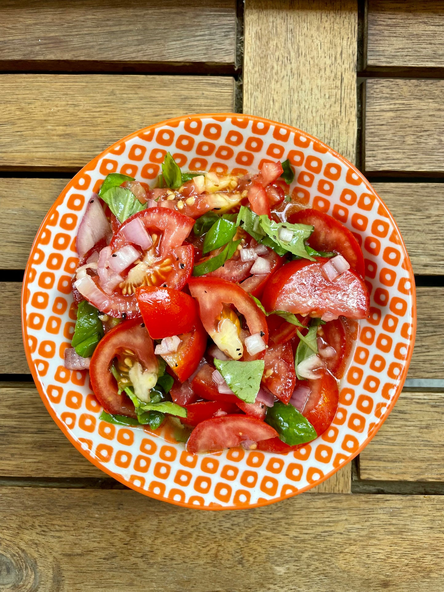Tomato salad drizzled with olive oil  on an orange patterned plate on a wooden surface