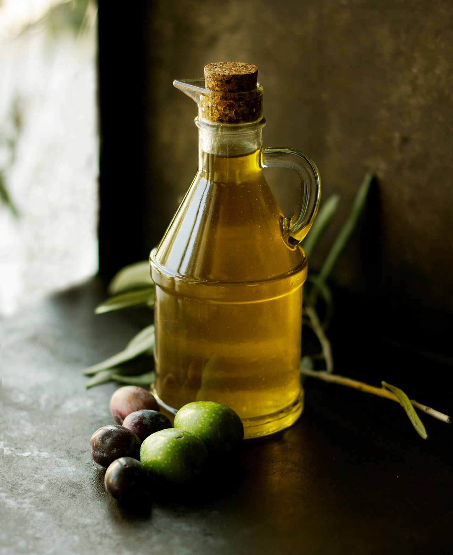 decanter of olive oil with fresh olives in foreground